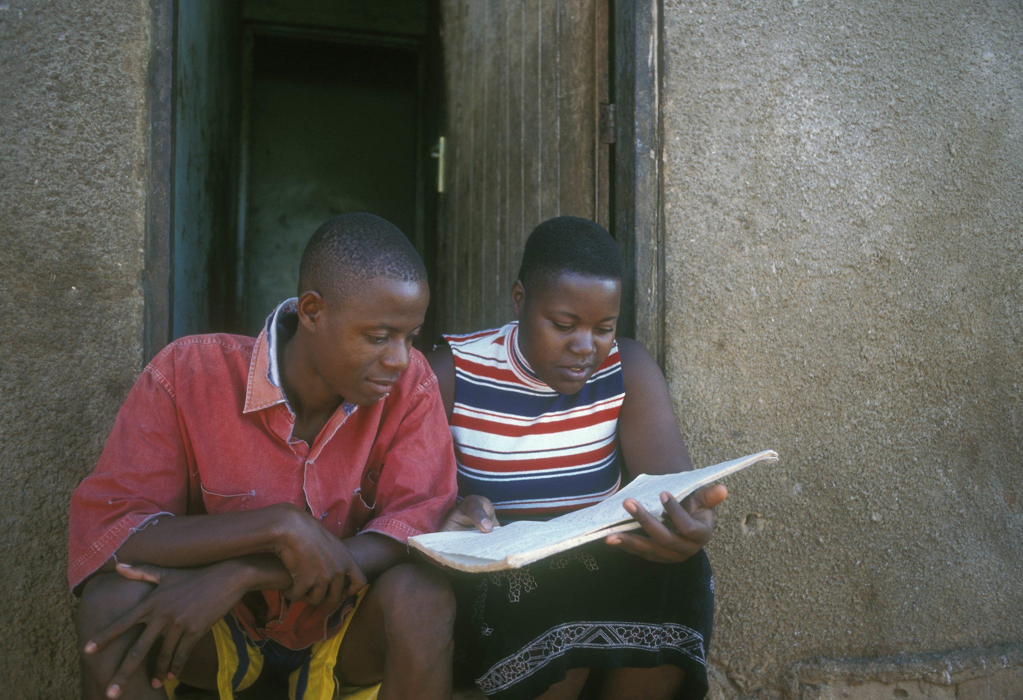 Teenage girl and boy in Uganda, looking at text book
