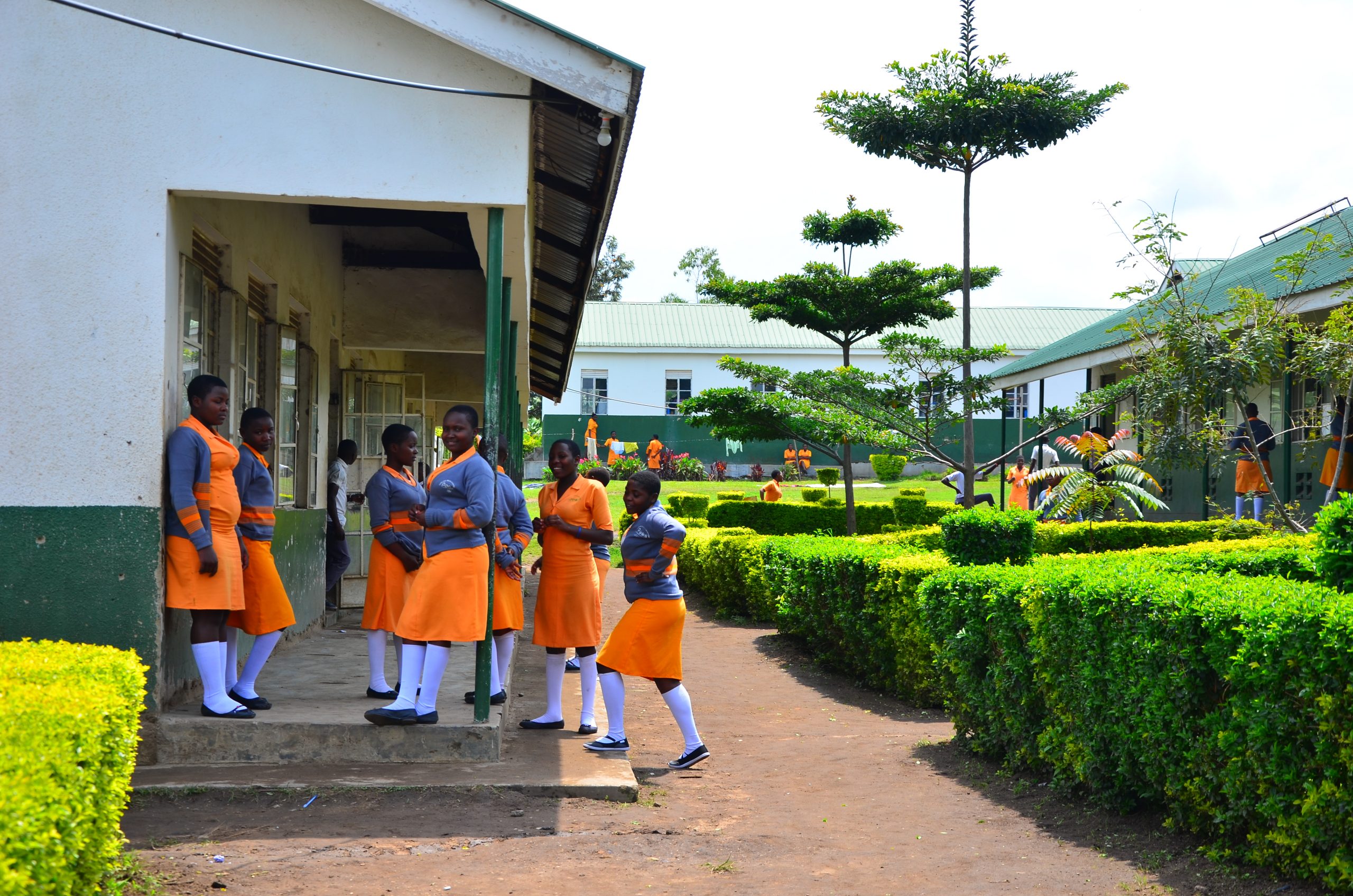 Teenage Ugandan school girls wearing orange and grey uniform outside a school building