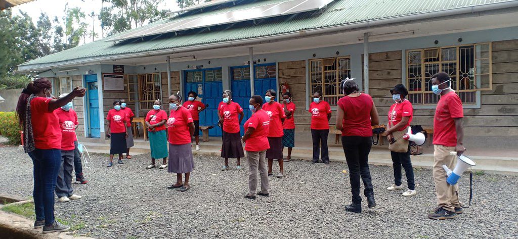 Briefing outside a school building. Socially distanced staff in face masks wearing red tshirts.