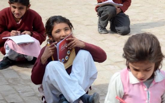 School children sitting on the ground with books