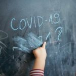 Child's hand on chalkboard on which is written COVID-19