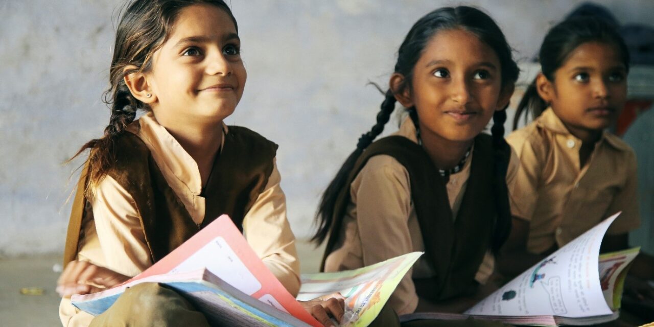 Three young Indian school pupils sitting on the floor with text books on their laps