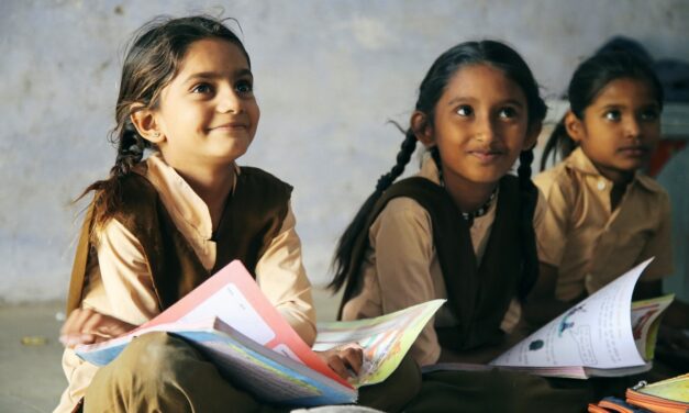 Three young Indian school pupils sitting on the floor with text books on their laps