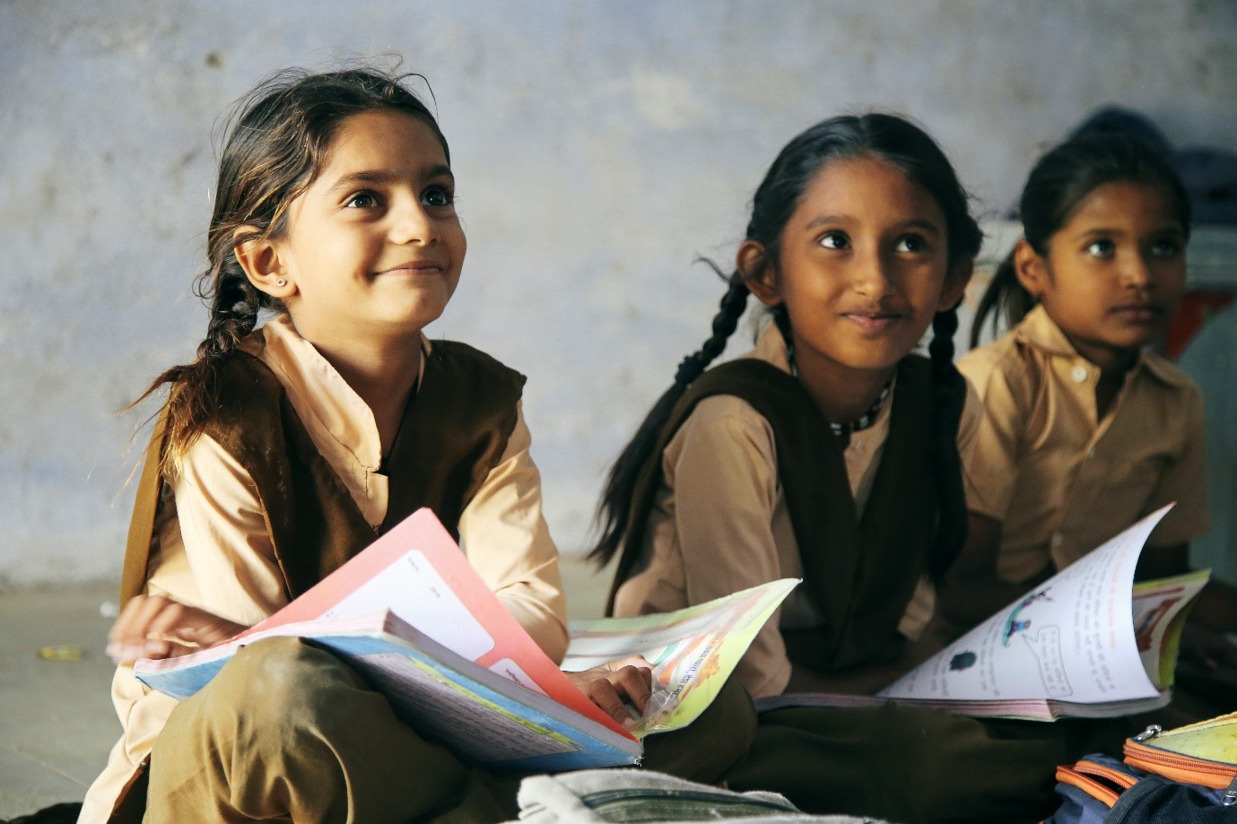 Three young Indian school pupils sitting on the floor with text books on their laps