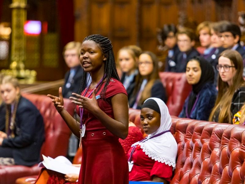 Young black woman standing and speaking among other school children