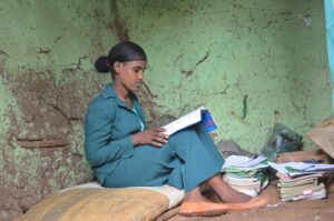 An Ethiopian grade 9 female student reading with a pile of books