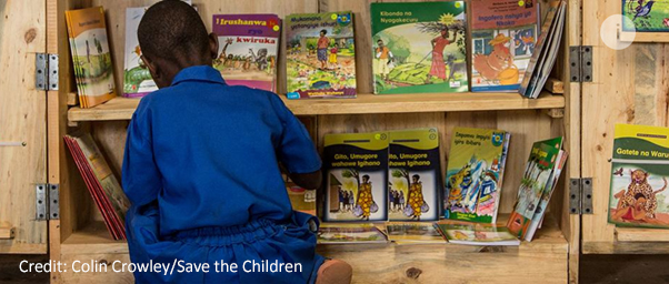 A Rwandan school child choosing a book from a cabinet shelf.