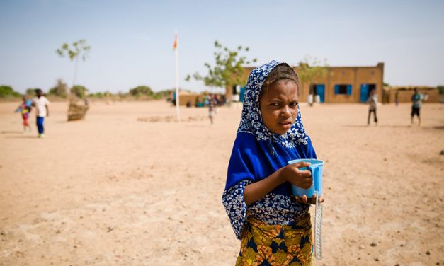 Girl with a cup outside a school building