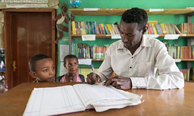 teacher marking two children in to register in a classroom