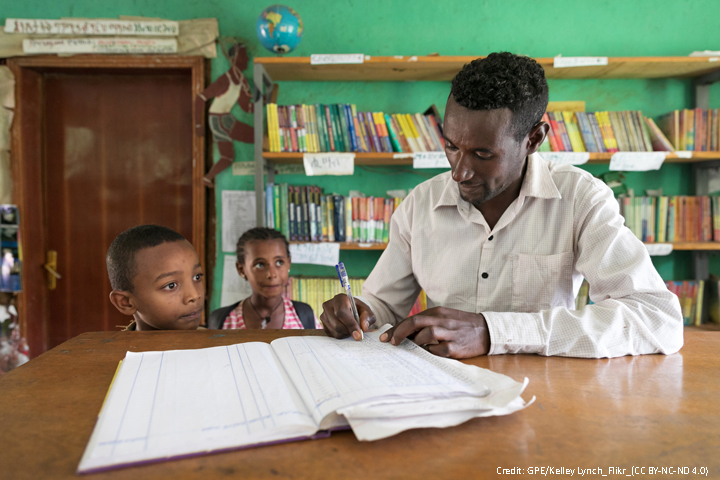 teacher marking two children in to register in a classroom