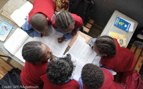 View from above of five children working on sheets and with textbooks in a classroom.