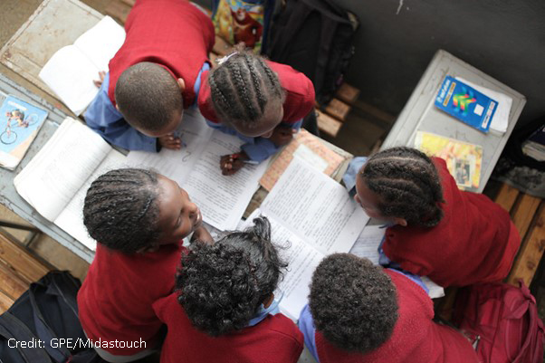 View from above of five children working on sheets and with textbooks in a classroom.