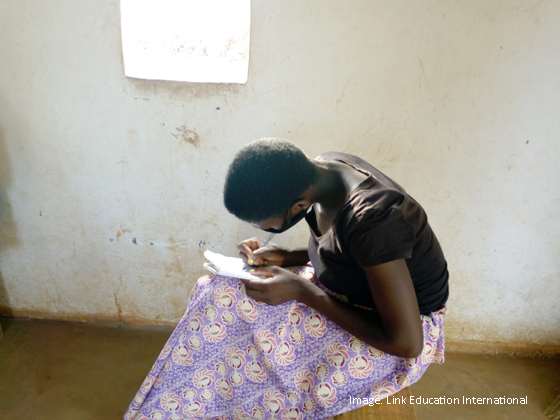 girl sitting writing, she is wearing a facemask