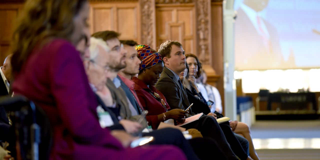 Side view of audience at Plenary of UKFIET Conference 2019 showing large screen through an open doorway with a speaker making the address