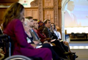 Side view of audience at Plenary of UKFIET Conference 2019 showing large screen through an open doorway with a speaker making the address