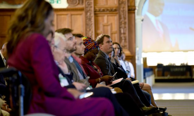 Side view of audience at Plenary of UKFIET Conference 2019 showing large screen through an open doorway with a speaker making the address