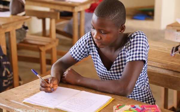 A girl working at a desk in Cote d'Ivoire, she is wearing a checked dress