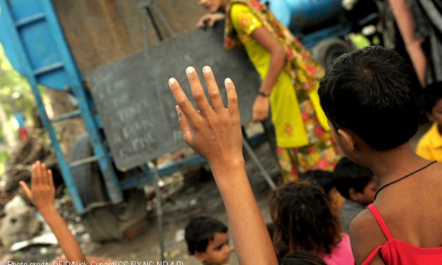 Hands up in class with a teacher and blackboard in the background