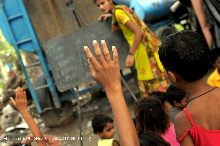 Hands up in class with a teacher and blackboard in the background