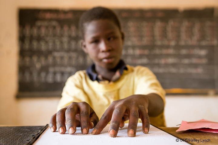 Blind child in a yellow top reading braille in a classroom