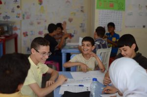 Syrian refugee boys sitting at table in class in Lebanon.  Smiling and learning.