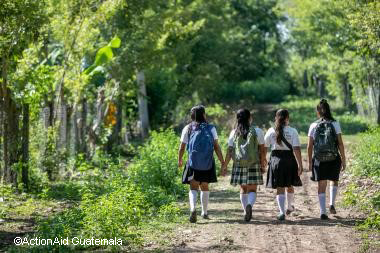 Four school girls walking along a track with trees either side in Guatamala