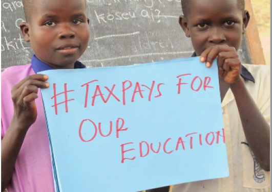 Ugandan boys holding up a sign saying #TAX PAYS FOR OUR EDUCATION