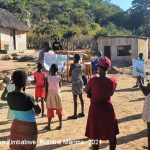 Teaching volunteer holds an informal community learning circle class outside in a rural village with social distancing and masks, Zimbabwe.