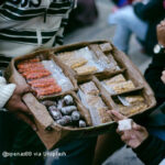 Informal street seller with box of small packets of sweets and dried fruit.