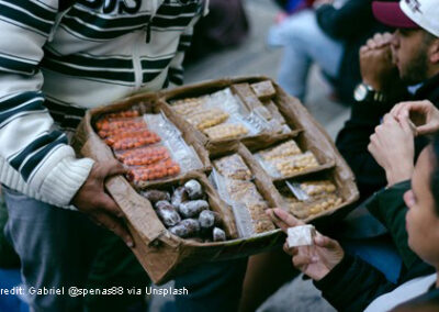Informal street seller with box of small packets of sweets and dried fruit.