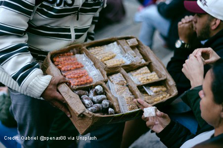 Informal street seller with box of small packets of sweets and dried fruit.