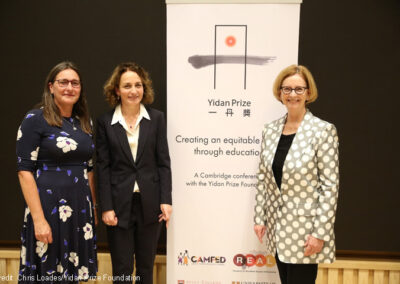 Pauline Rose from the REAL Centre, Lucy Lake from CAMFED and the Honourable Julia Gillard stand in front of a conference banner for the Yidan Prize Foundation conference organised by the REAL Centre and CAMFED on 7 October 2021.