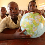 A girl student holds a globe of the world in class pointing to Sierra Leone