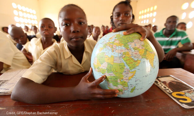 A girl student holds a globe of the world in class pointing to Sierra Leone