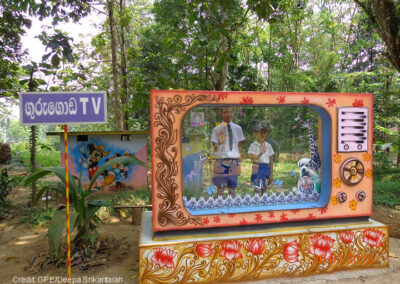 Two boys stand behind a large mock TV to pretend to be on air in a maths park in Sri Lanka.