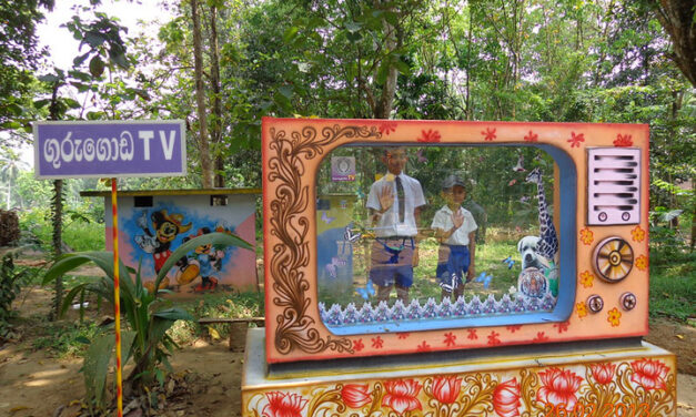 Two boys stand behind a large mock TV to pretend to be on air in a maths park in Sri Lanka.