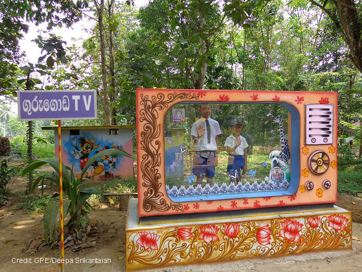 Two boys stand behind a large mock TV to pretend to be on air in a maths park in Sri Lanka.