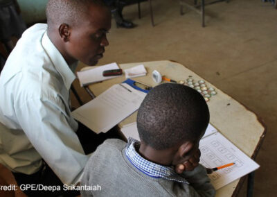 Enumerator sits with a young boy in a classroom and administers the Early Grade Mathematics Assessment (EGMA) in Marikani Government School, Nairobi, Kenya.