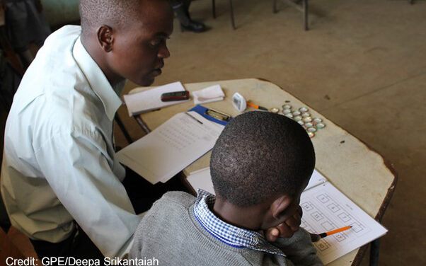 Enumerator sits with a young boy in a classroom and administers the Early Grade Mathematics Assessment (EGMA) in Marikani Government School, Nairobi, Kenya.