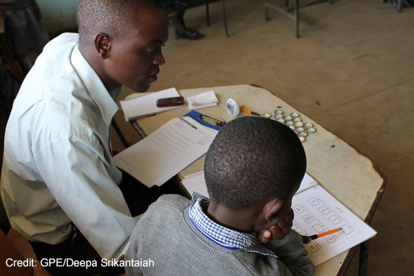 Enumerator sits with a young boy in a classroom and administers the Early Grade Mathematics Assessment (EGMA) in Marikani Government School, Nairobi, Kenya.