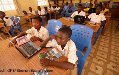 Children sit two to a desk with a laptop to share between them in computer class, Gbimsi Junior High School, Savelugu, Northern Region Ghana.