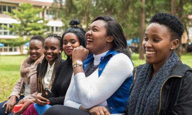 Group of young women laughing on a bench outside their university.