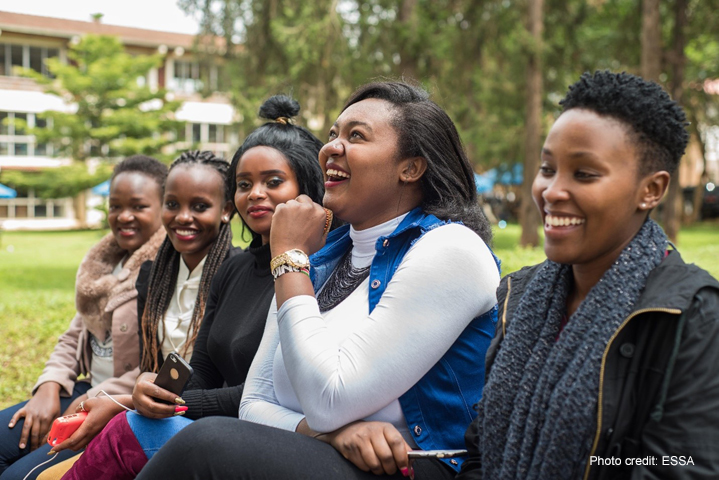 Group of young women laughing on a bench outside their university.