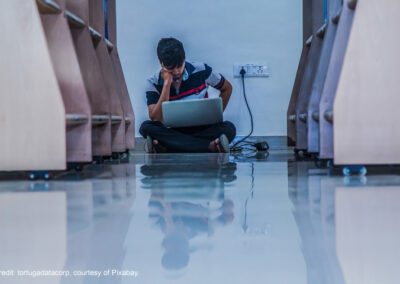 Male adult student studies with laptop plugged in on the floor of a library, in Pune, India.