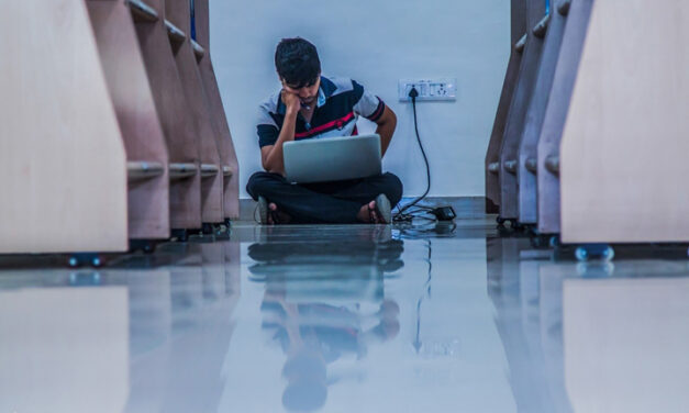 Male adult student studies with laptop plugged in on the floor of a library, in Pune, India.