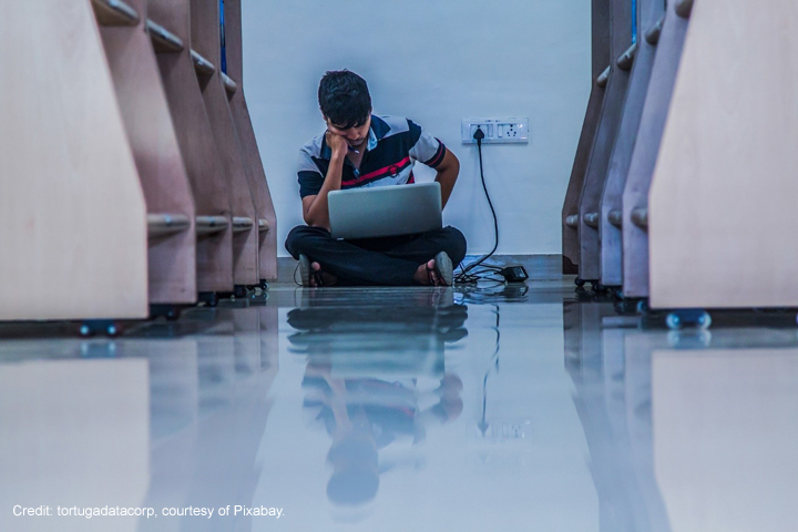Male adult student studies with laptop plugged in on the floor of a library, in Pune, India.