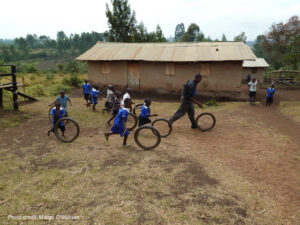 Primary school children chase bicycle tyres across the school yard with their teacher at a remote school in Uganda.