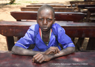 Image of Sagal, a boy sitting on a desk in the school yard. Sagal lives with his mother and three siblings in North East Uganda. The region is experiencing severe drought and many families are struggling to feed their children. Save the Children is providing school meals to help children stay in school and continue to learn.