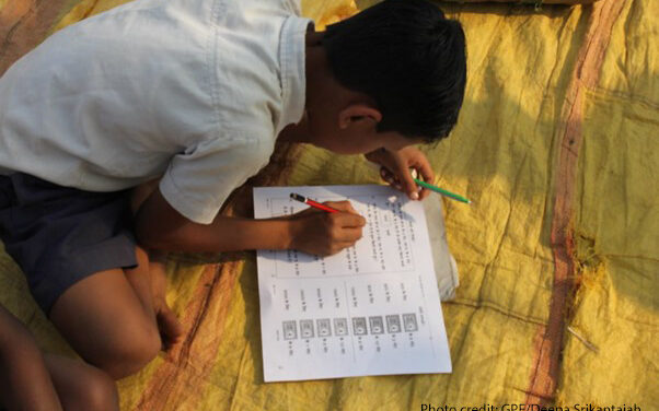 Boy sits on a rug studying with his workbook, India.