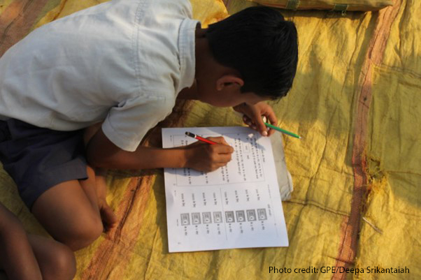 Boy sits on a rug studying with his workbook, India.